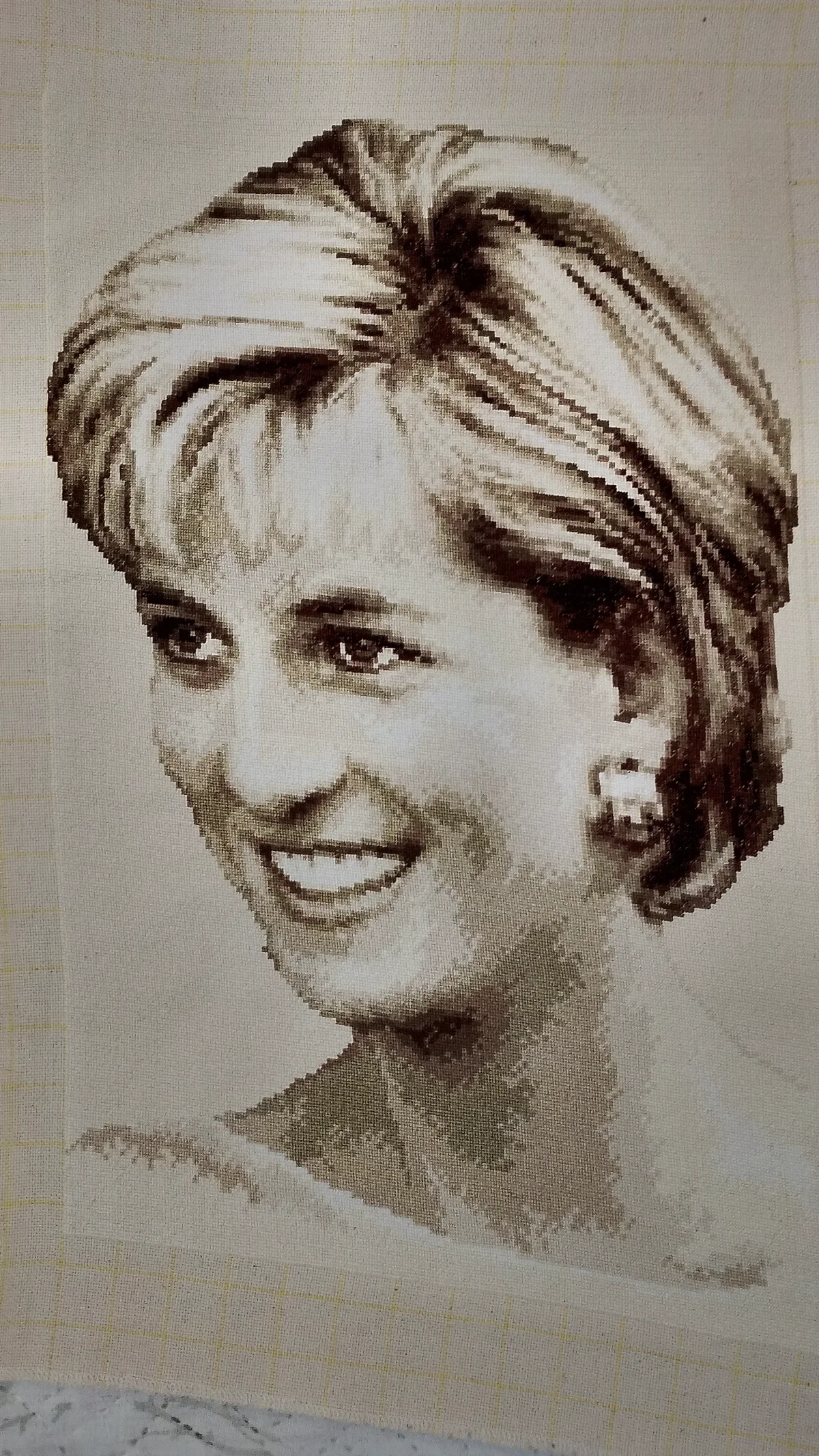 Retrato bordado marrón y crema de una princesa Diana sonriente, con cabello peinado hacia un lado y pendiente cuadrado