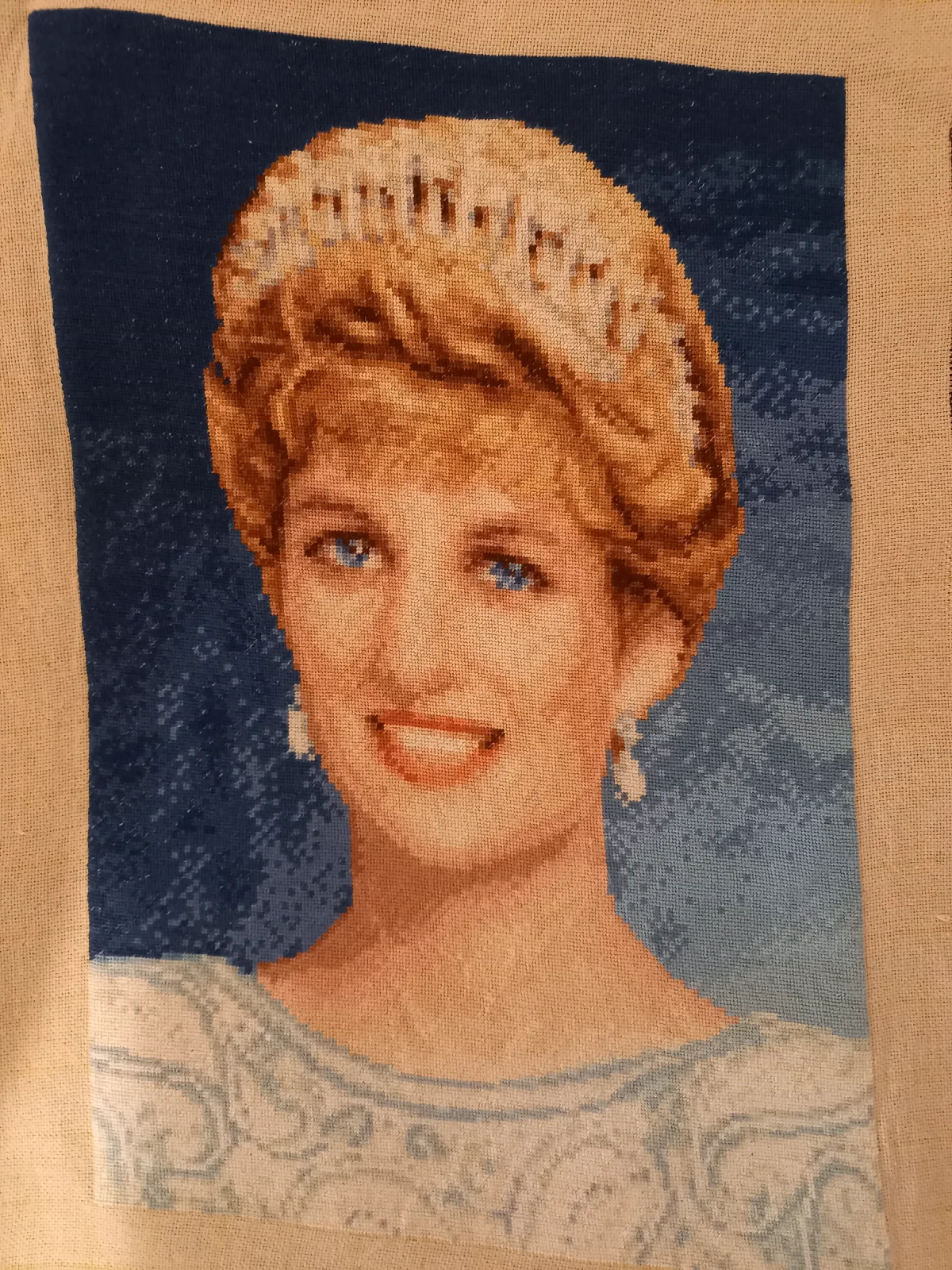 Ritratto ricamato della principessa Diana con tiara, occhi azzurri e abito chiaro su sfondo blu marino
