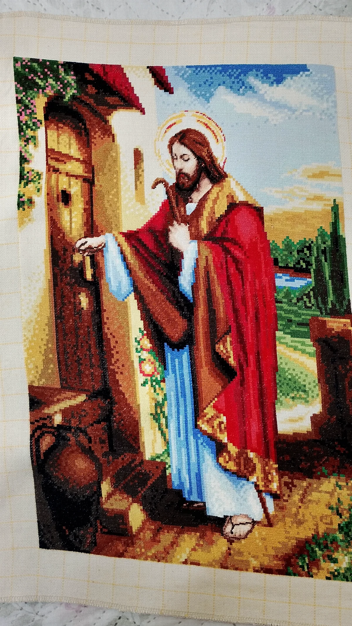 Jesús extendiendo la mano hacia una puerta de madera, con túnica azul, manto rojo y flores cercanas