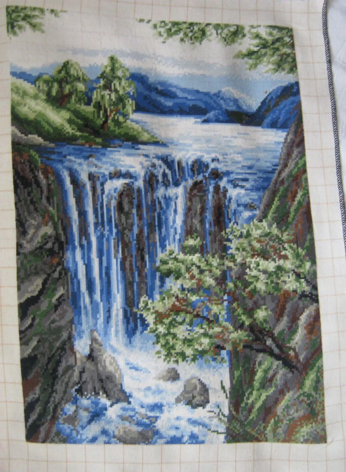 Multiple blue-white cascades descending between rocks beneath a lake and distant hills